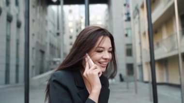 Genç iş kadını gülümsüyor, akıllı telefondan konuşuyor.