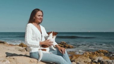 Genç yetişkin bir kadın kumsalda küçük bir köpekle vakit geçiriyor.