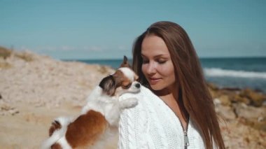 Genç yetişkin bir kız, kumsalda küçük bir köpekle vakit geçiriyor.