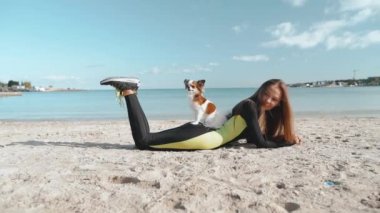 Genç yetişkin atletik kız günü sahilde küçük bir köpekle geçiriyor.