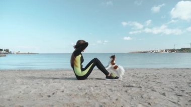 Genç ve sportif kız deniz kenarında köpekle antrenman yapıyor.