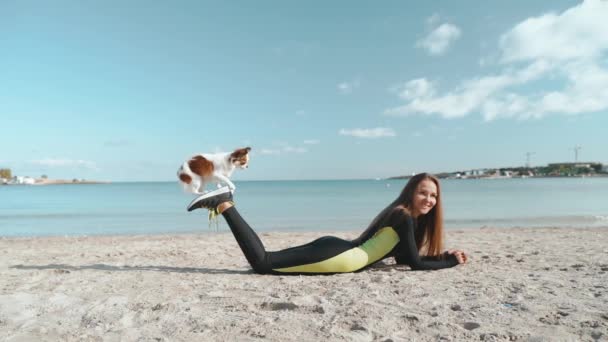 Młoda dorosła sportowiec kobieta bawi się z małym zwierzakiem na plaży — Wideo stockowe