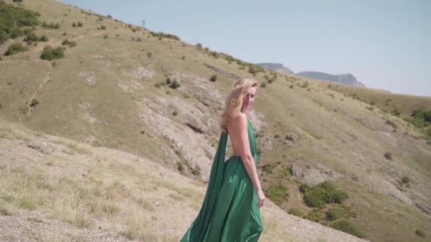 Молодая взрослая женщина стоит на холме в модном зеленом платье — стоковое видео