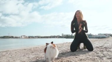 Genç sporcu kadın deniz kenarında küçük bir köpek eğitiyor.