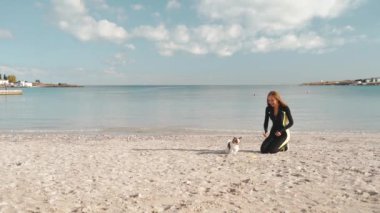 Genç sporcu kadın deniz kenarında küçük bir köpekle oynuyor.