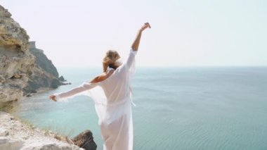 Genç bir kadın kayalık tepede denize bakıyor.