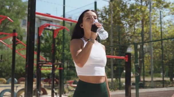 Young adult sporty woman drinking water after training outdoors — 图库视频影像