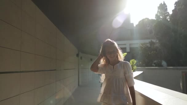 Jugendliches Mädchen in Brille spaziert durch die Stadt und lächelt breit — Stockvideo