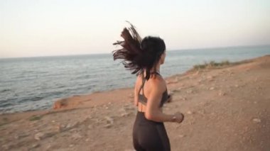 Genç bayan sporcu açık havada antrenman yapıyor, deniz kenarında koşuyor.