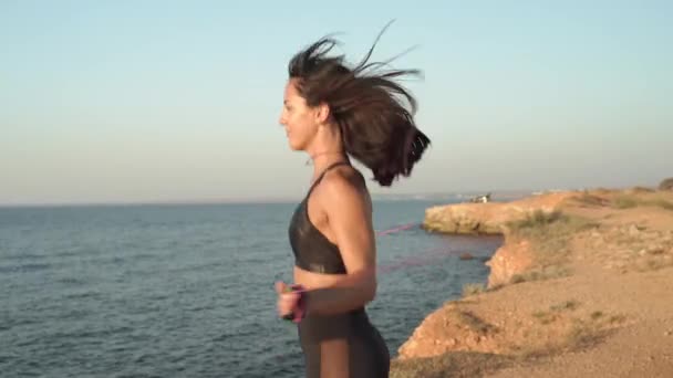 Young adult athlete girl training near sea with jumping rope — Stock Video