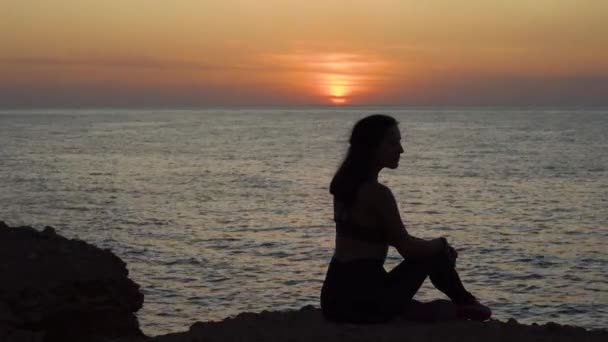 Ung vuxen kvinna sitter nära havet, tittar på solnedgången — Stockvideo