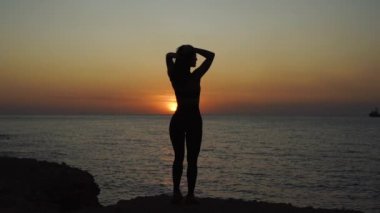 Young adult girl with perfect body looking at sunset near sea