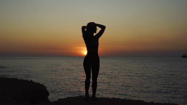 Młoda dorosła dziewczyna z idealnym ciałem patrząc na zachód słońca w pobliżu morza — Wideo stockowe