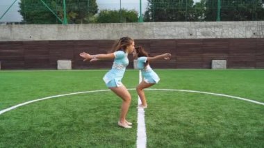 Two young girls in cheerleader in uniform support university sport team, making flip back