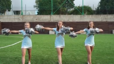 Teenage girls in cheerleaders uniform with pom poms support sport team
