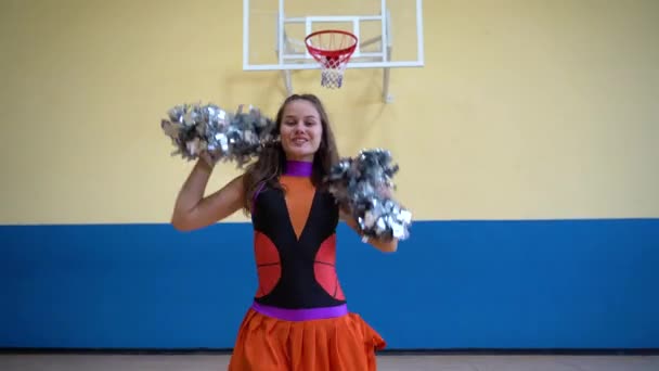 Young girl in cheerleader uniform with pom poms support high school sport team — Stock video