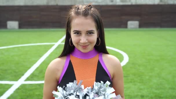 Cheerleader girl in uniform with pom poms looking at camera — ストック動画
