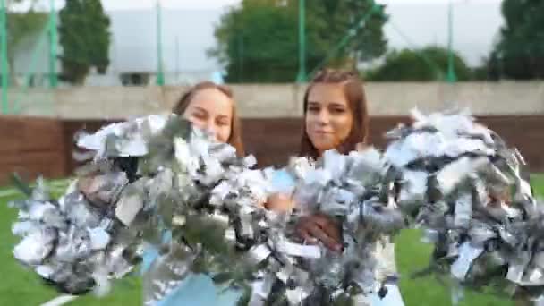 Девочки-подростки в форме болельщиц трясутся с помпонами, поддерживают университетскую спортивную команду — стоковое видео