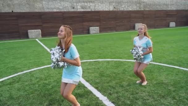 Two cheerleaders girls in uniform with pom poms support high school sport team — Stockvideo