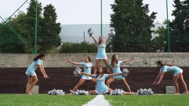 Cheer leaders girls in uniform with pom poms making acrobatic figure together — Wideo stockowe