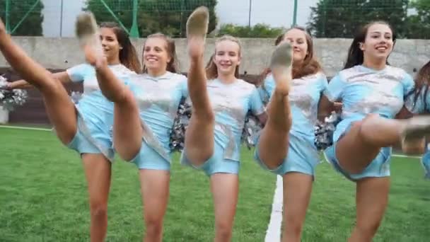 Девушки в форме группы поддержки с помпонами поддерживают спортивную команду в колледже — стоковое видео