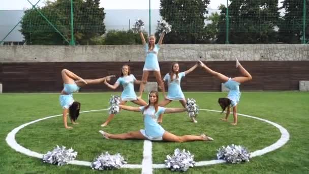 Chicas jóvenes en porrista en uniforme con pompones haciendo figura acrobática juntos — Vídeo de stock