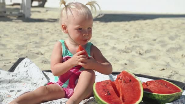 Little child girl sitting on beach with watermelon in hand — Stock Video