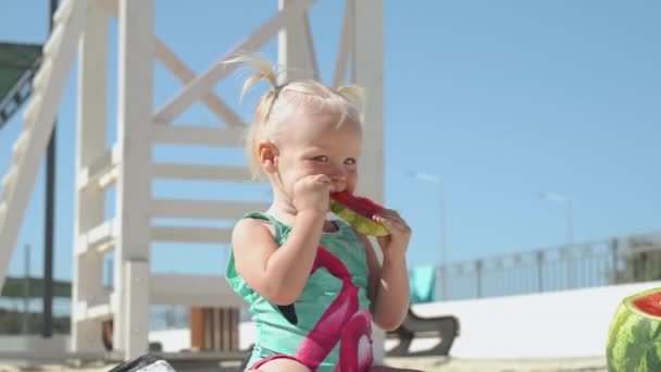 Klein meisje eten watermeloen, zitten op het strand — Stockvideo