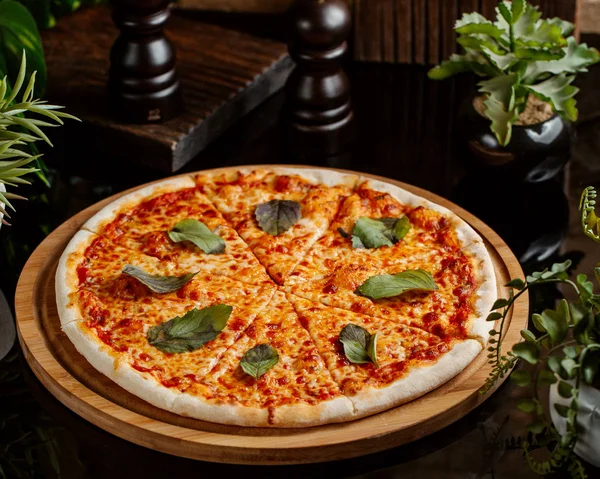 Pizza de margarita cubierta con hojas de albahaca servidas en pizza de madera —  Fotos de Stock