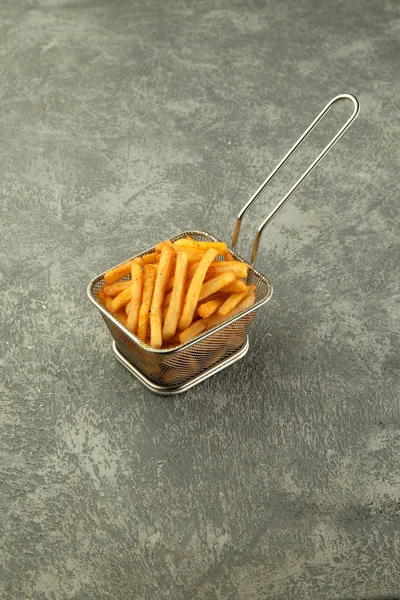 steel basket of french fries on plain grey background