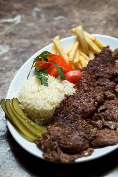 beef kebab plate with french fries, cucumber pickles, rice and
