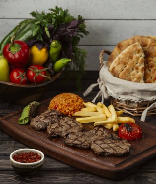 Izgara biftek parçaları, bulgur, ızgara sebze ve patates kızartması.