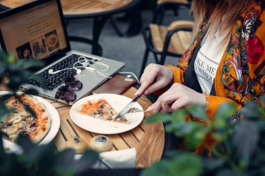 Kadın bir kafede çatal ve bıçakla pizza dilimi kesiyor.