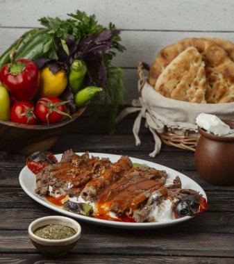 İskender kebabı domates sosu ve yoğurt ile süslenmiş, ızgara sebzelerle servis ediliyor.