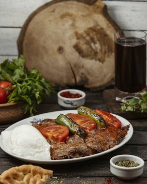 İskender kebabı domates sosuyla süslenmiş, biber, yoğurtla servis edilmiş.