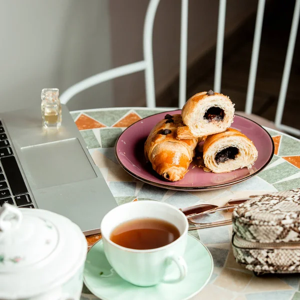 close up to round table with chocolate croissant tea cup_ notebook and bag
