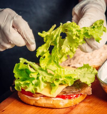 Şef peynirli ve domatesli marul ekleyerek hamburger hazırlıyor.