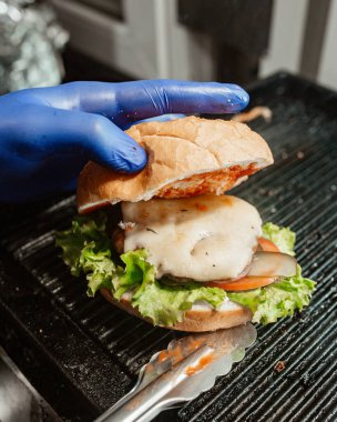 Şefin elinde erimiş peynirli, soğanlı, salatalıklı ve salatalıklı sığır burger var.