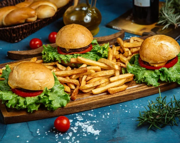Tre små biffburgare och pommes frites serveras på träskiva — Stockfoto