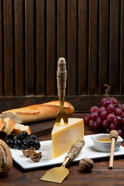 Morceau de fromage parmesan avec fourchette au fromage sur le dessus, servi avec du miel, raisin — Photo