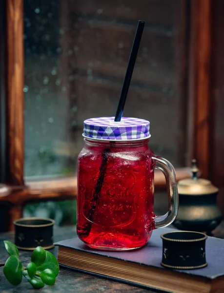 Iced pink drink in mason jar with black straw in front of the window