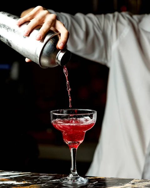 Bartender pours red cocktail into a glass with long stem — Stock Photo, Image