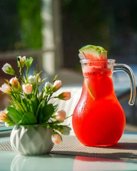 Karaff med kall vattenmelonsaft och en vas med blommor — Stockfoto