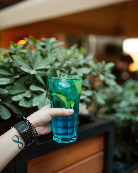 Žena drží sklenici modrého mojito s mátovým lístkem a citrónem — Stock fotografie