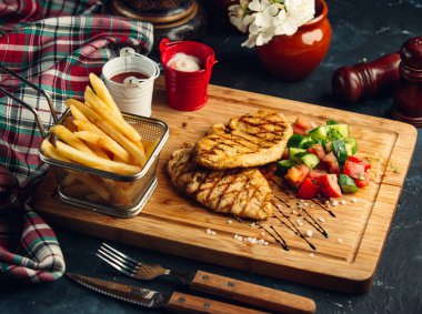 Izgara tavuk fileto yanında salata, patates kızartması, mayonez ve ketçap.