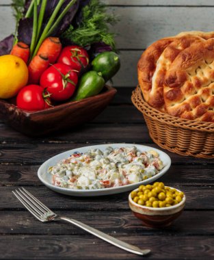 Beyaz küçük tabakta yeşil bezelyeyle servis edilen olivier salatası.