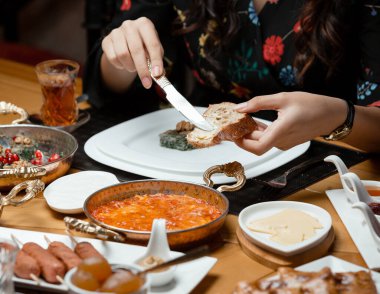 Geleneksel kahvaltı düzeninde kadın ekmeğe tereyağı sürüyor.