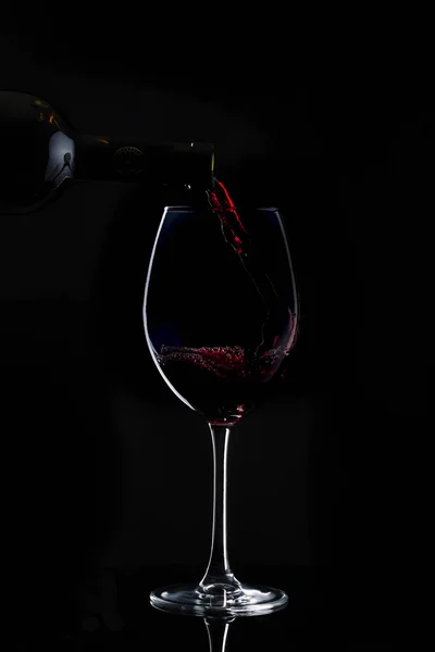 Vinho tinto está sendo derramado em vidro com haste longa no escuro — Fotografia de Stock