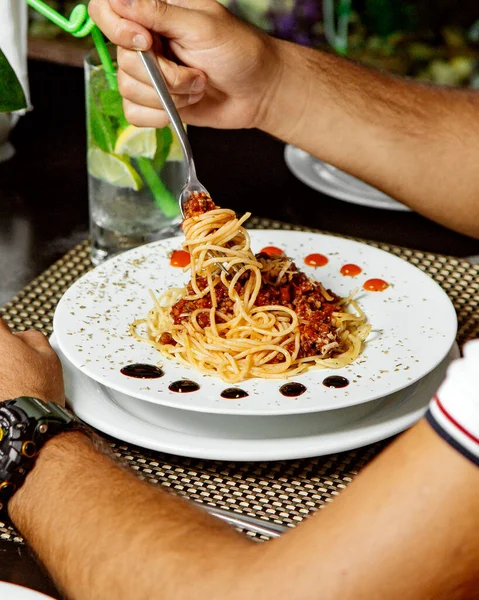 Man eating spaghetti bolognese garnished with dried mint leaves — Stock Photo, Image