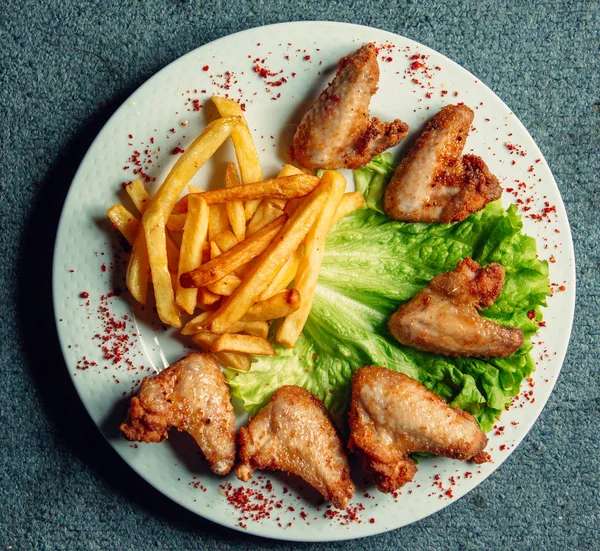 Horní pohled na grilovaná kuřecí křidýlka podávaná na listech salátu s hranolky — Stock fotografie